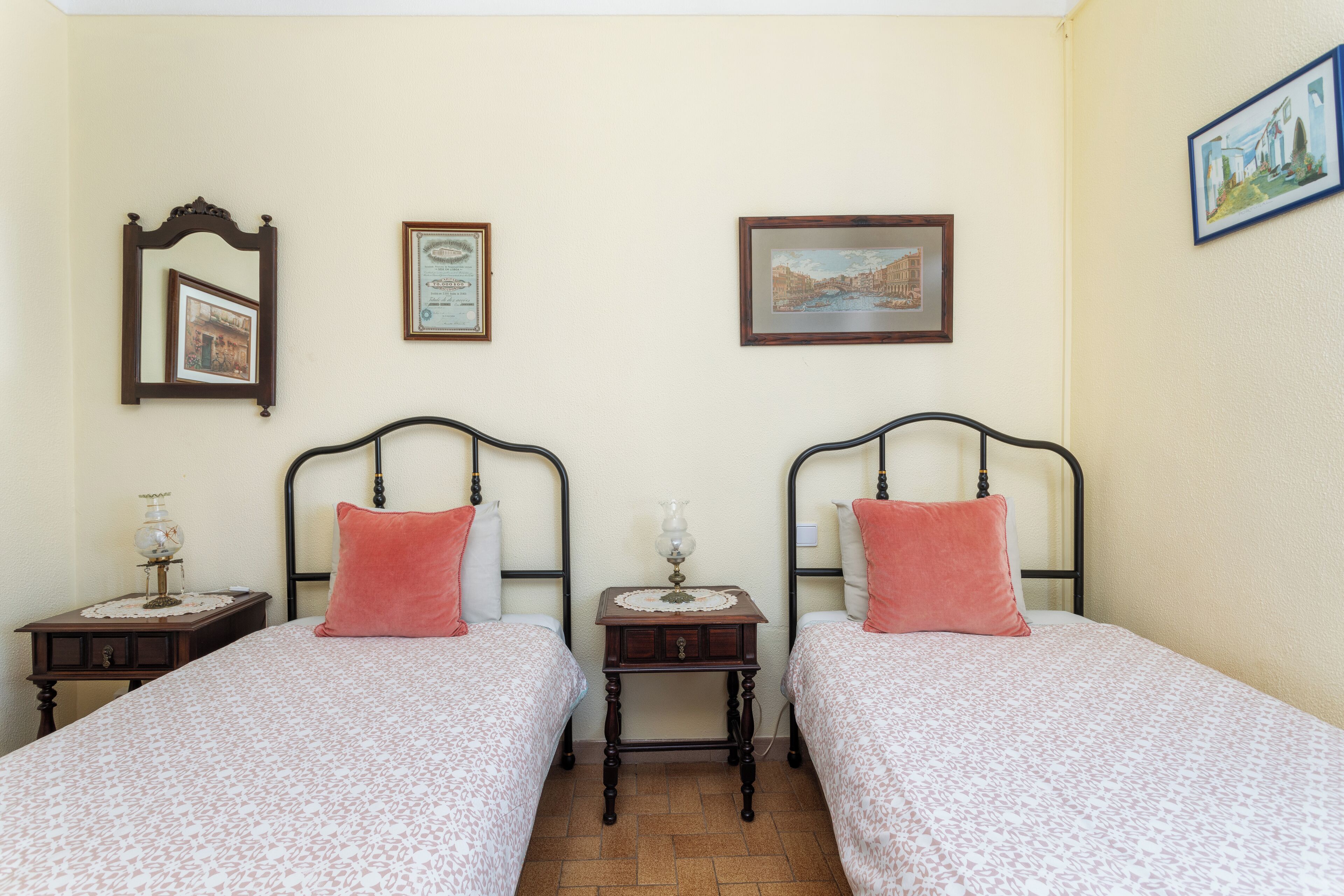 A room with two beds, each with a matching headboard, a small bedside table with a lamp, and a framed certificate on the wall.