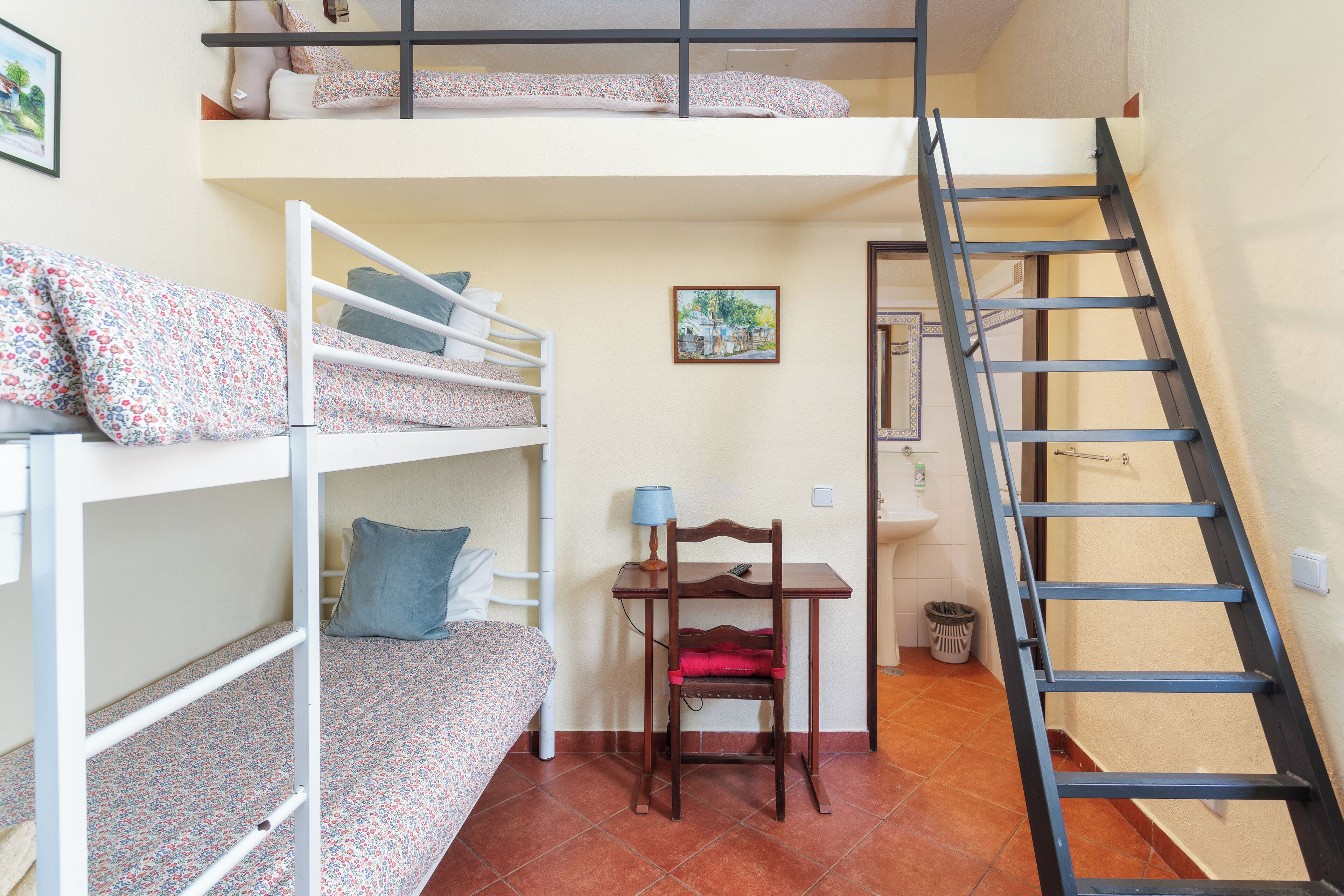 A dormitory room with bunk beds, a desk, a chair, and a ladder.