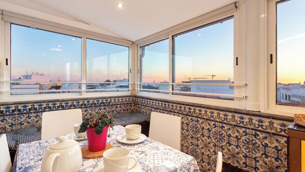 Un comedor con una mesa dispuesta para dos personas, una planta en maceta y vistas de la ciudad a través de amplios ventanales.