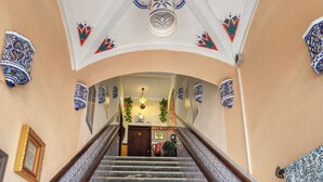 Una gran escalera con intrincados diseños de azulejos blancos y azules en las paredes y los peldaños, que conduce a una zona de recepción con un mostrador de madera y un cuadro en la pared.