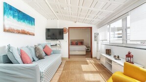 Una sala moderna con un sofá, una butaca amarilla, un televisor y una cama al fondo.
