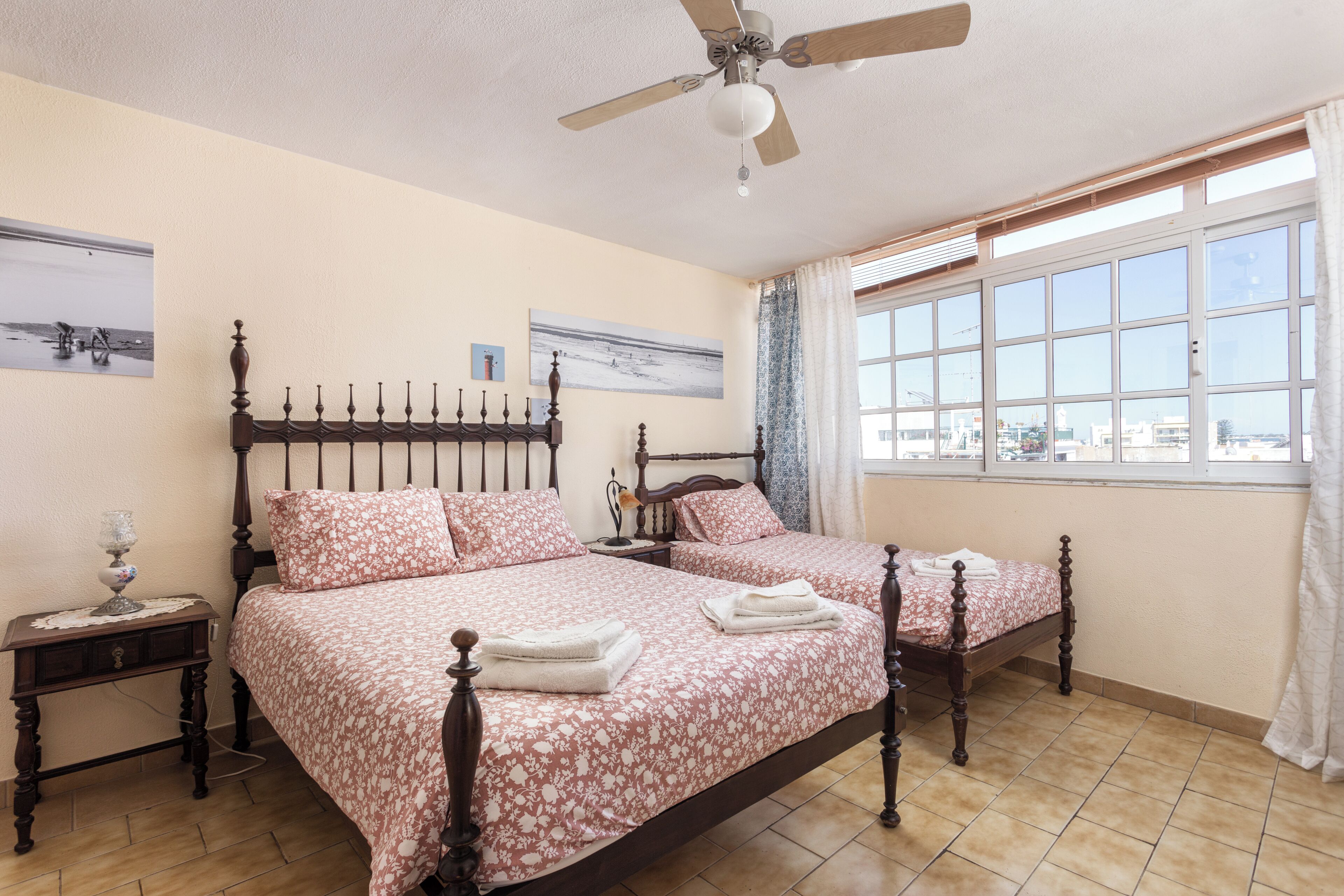 Une chambre avec deux lits, un ventilateur de plafond, une table de chevet avec une lampe et une fenêtre avec des rideaux.