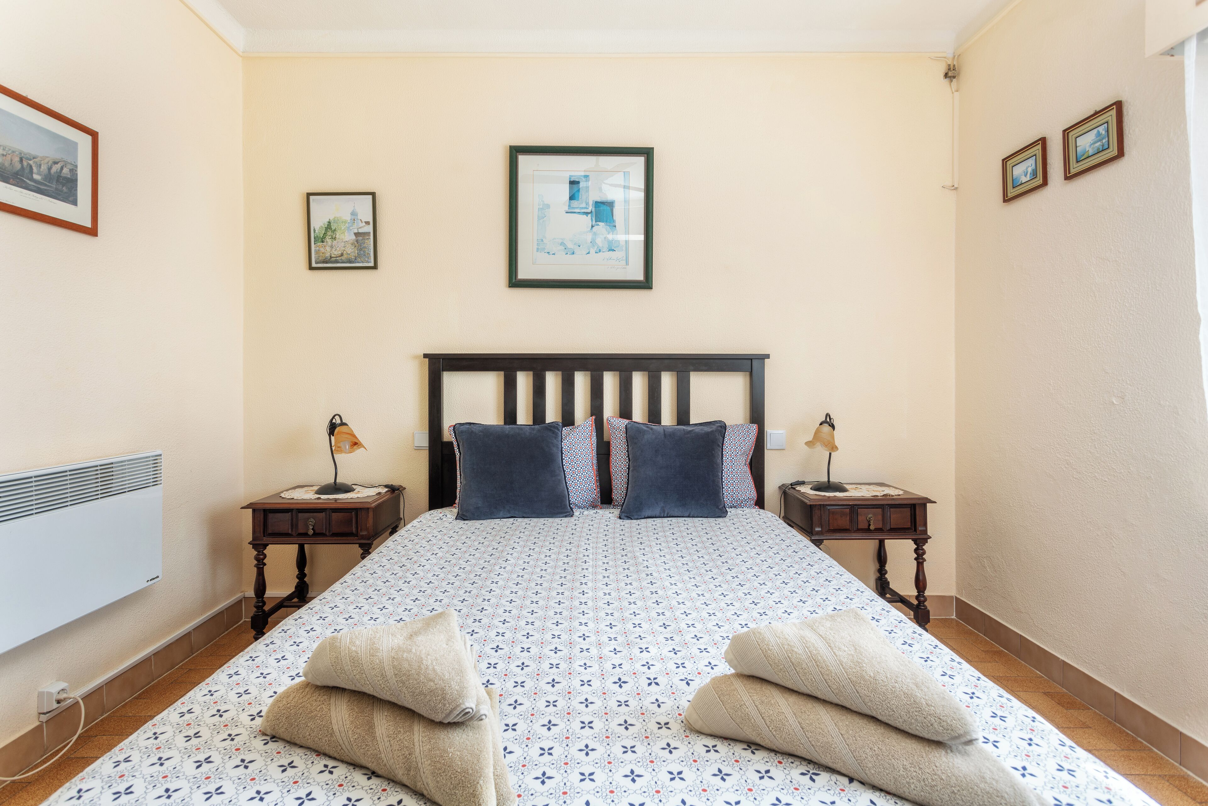 A neatly arranged bedroom with a bed, two bedside tables, and a wall-mounted heater.