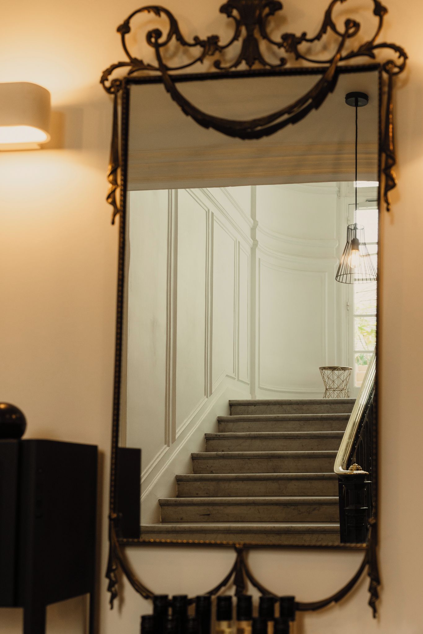 A mirror with an ornate frame reflecting a staircase and a chandelier.
