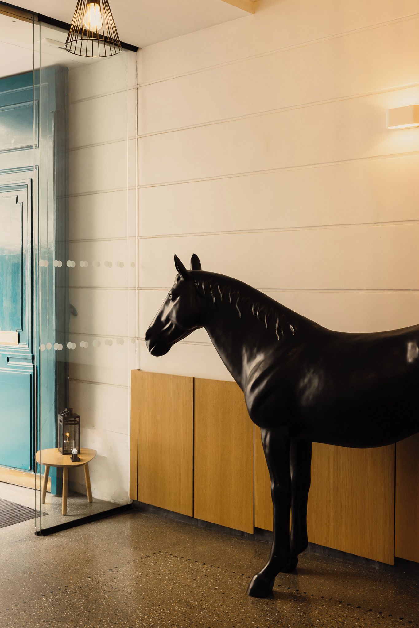 Una estatua de un caballo negro en una habitación con un aparador de madera y una pequeña mesa con un farol.