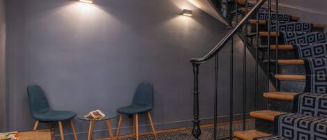 A staircase with patterned steps, two blue chairs, a small table with a book, and a herringbone-patterned floor.