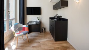 A compact kitchen with a modern design, a dining area with a patterned chair, and a large window providing natural light. -  Hotel Helzear Etoile (Paris)