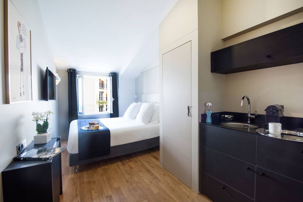 A modern hotel room with a bed, a desk, a sink, and a window with curtains.