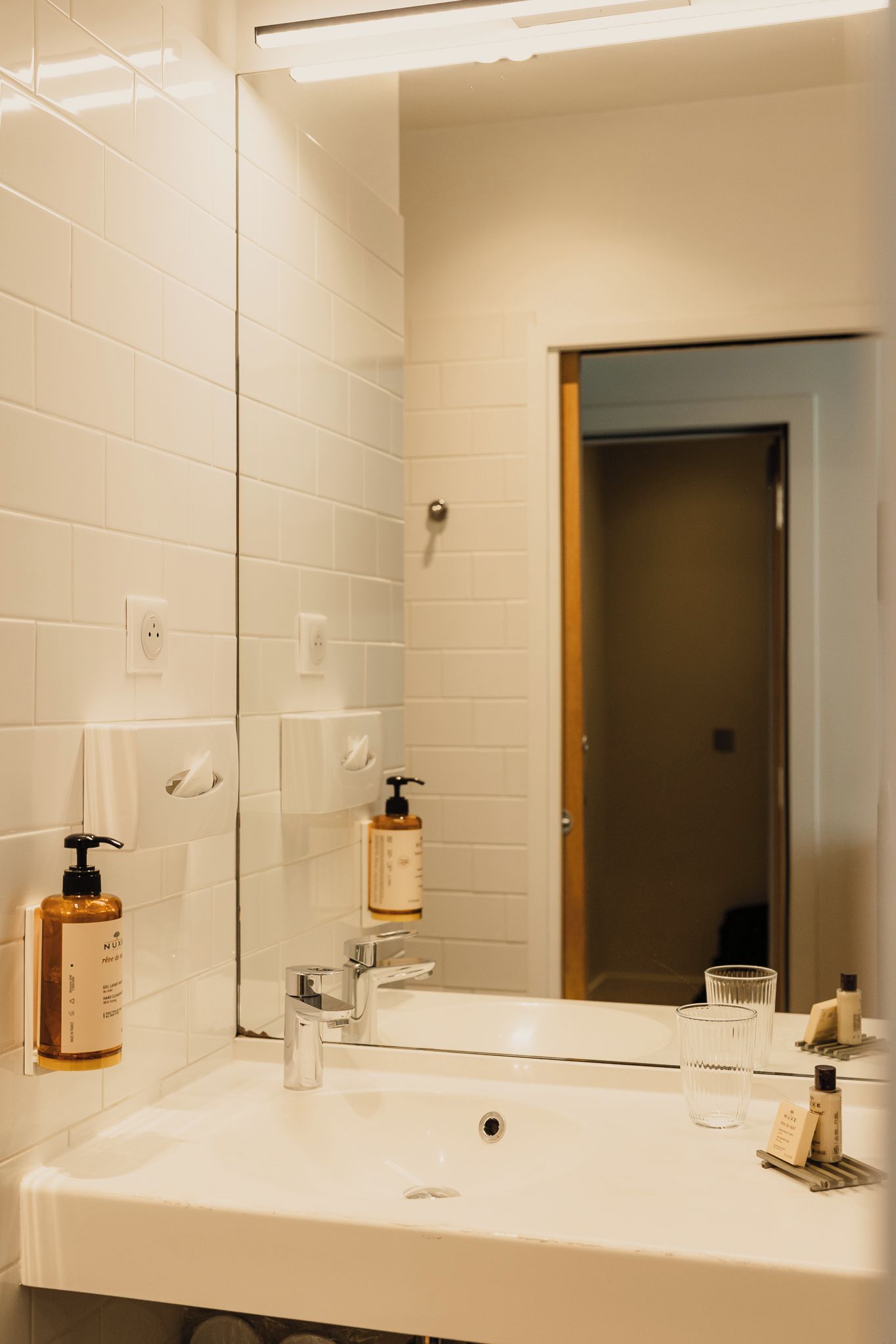 A bathroom with a white sink, a mirror, and a door leading to another room.
