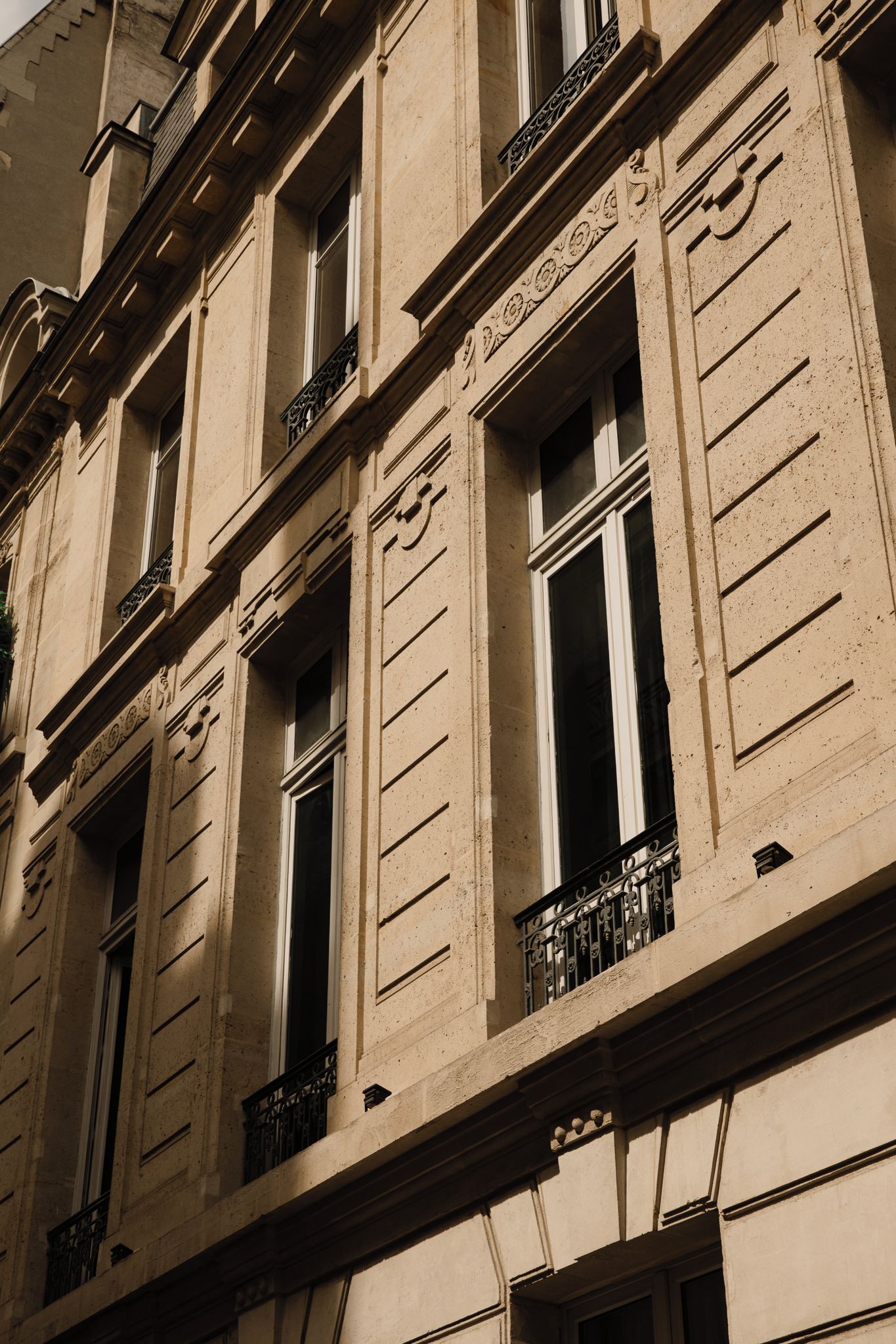 Une façade d’immeuble ornée de nombreuses fenêtres, de moulures décoratives et d’un balcon doté de balustrades en fer forgé.