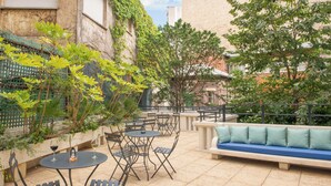 An outdoor patio with tables and chairs, a sofa, and a stone wall with greenery. -  Hotel Helzear Etoile (Paris)