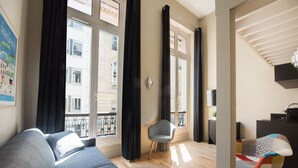 A modern living room with a grey sofa, a patterned armchair, and a round rug. -  Hotel Helzear Etoile (Paris)