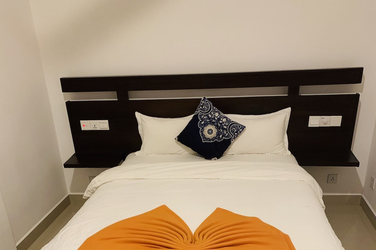 Un lit bien fait, avec une couette blanche et un coussin décoratif orange.