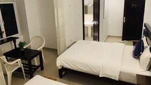 A hotel room with a bed, a desk with a chair, a mirror, and a door. - Lavenro Hotel & Resort (Deniyaya)
