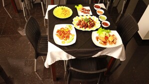 A dining table with various dishes, including noodles, a salad, and a sandwich, surrounded by black chairs. - Lavenro Hotel & Resort (Deniyaya)