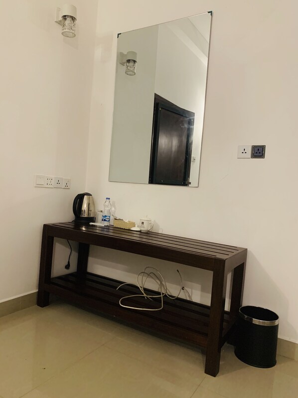 A small, clean room with a wooden console table, a mirror, a trash bin, and a wall socket.