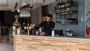A bar area with a wooden counter, shelves with bottles, and a cash register. - Arenahotellet i Uppsala (Uppsala)