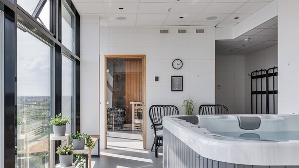 A modern hotel room with large windows, a hot tub, and a view of the city. - Arenahotellet i Uppsala (Uppsala)