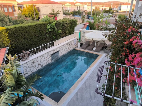 A rectangular swimming pool with a stone border, surrounded by a white metal fence. - Degirmenli Konak (Cesme)