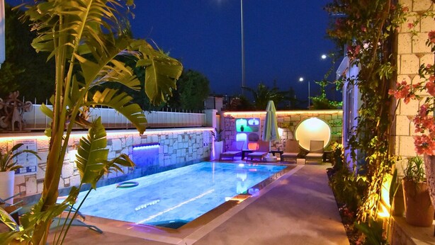 A swimming pool area with a stone wall, a lounge chair, and a small table. - Degirmenli Konak (Cesme)