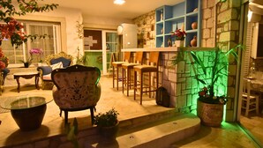 A cozy living area with a glass-top coffee table, a floral armchair, and a bar area with stools. - Degirmenli Konak (Cesme)
