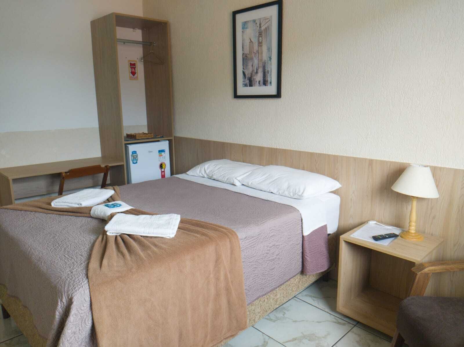 Una habitación de hotel con una cama, un escritorio, una silla, un armario y un refrigerador pequeño.