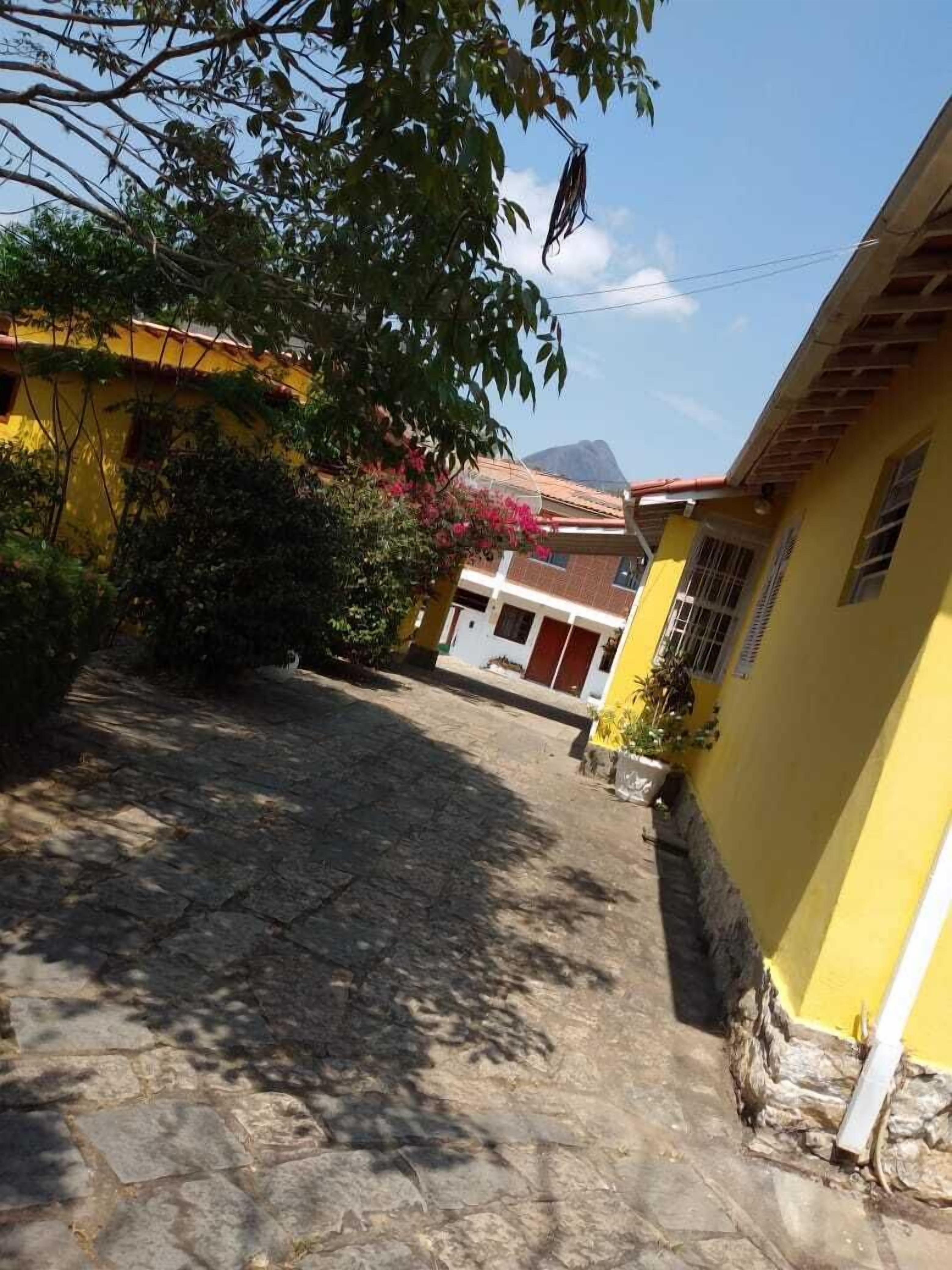 A narrow cobblestone street flanked by yellow buildings with red doors, leading to a mountain in the background.
