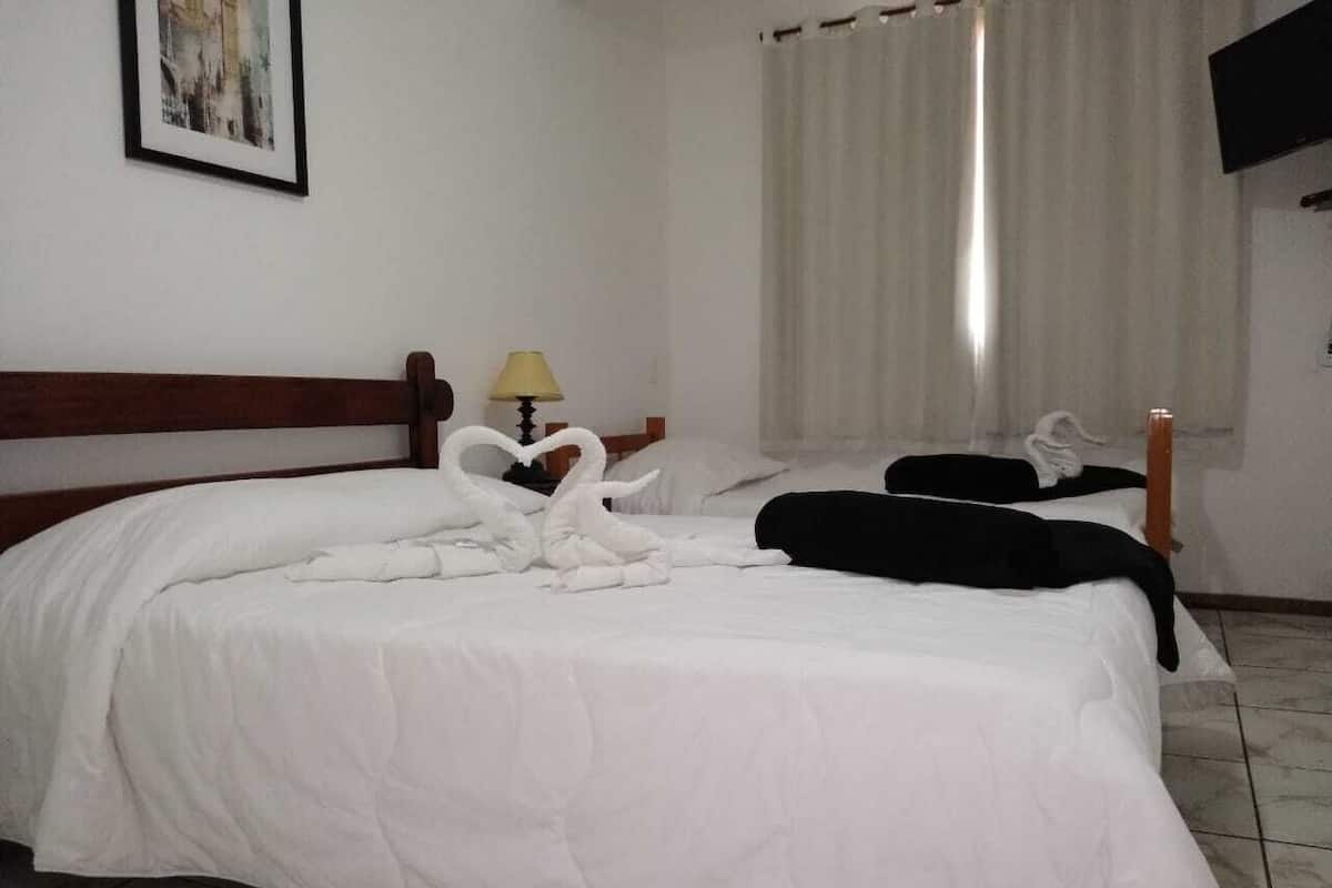 A hotel room with a large bed, a wooden headboard, a bedside table with a lamp, and a window with curtains.