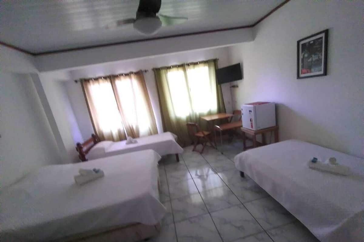 A hotel room with three single beds, a desk, a chair, and a television on the wall.