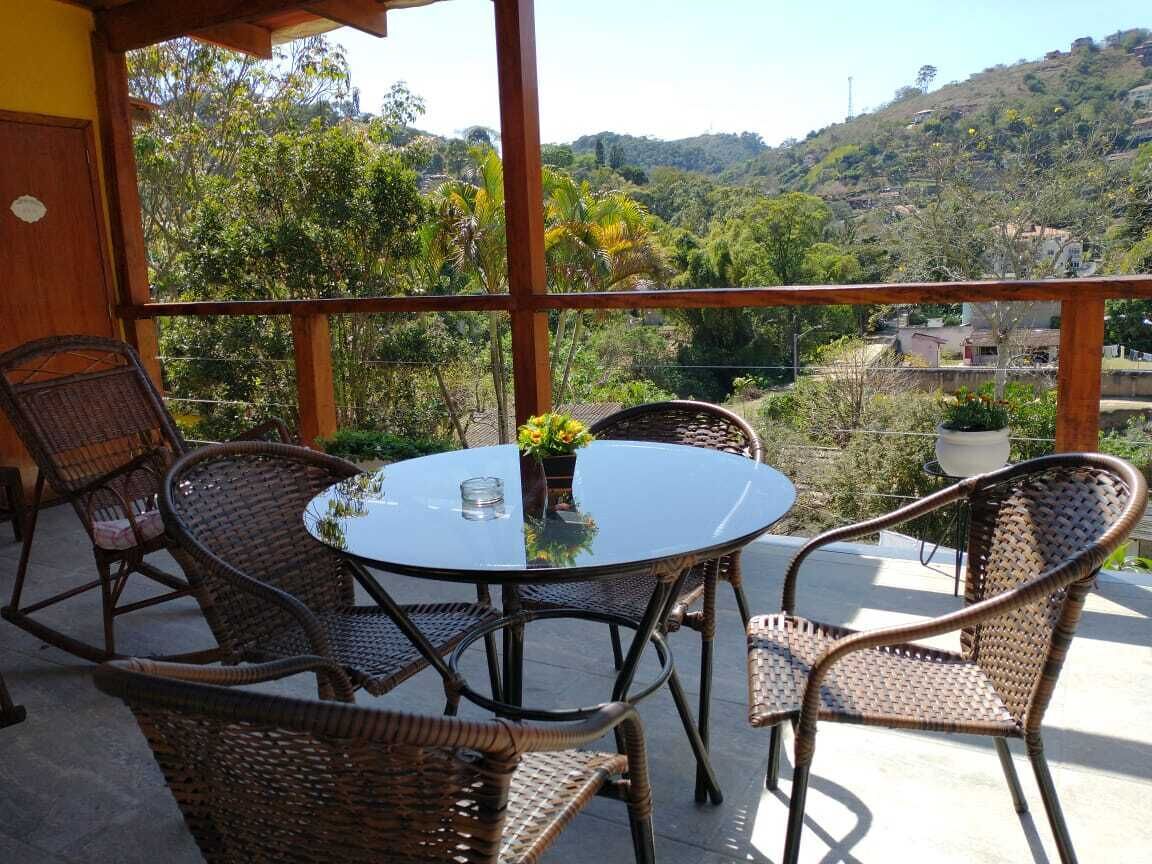 Un balcon agrémenté de meubles en osier et d’une table en verre, offrant une vue sur un paysage vallonné.