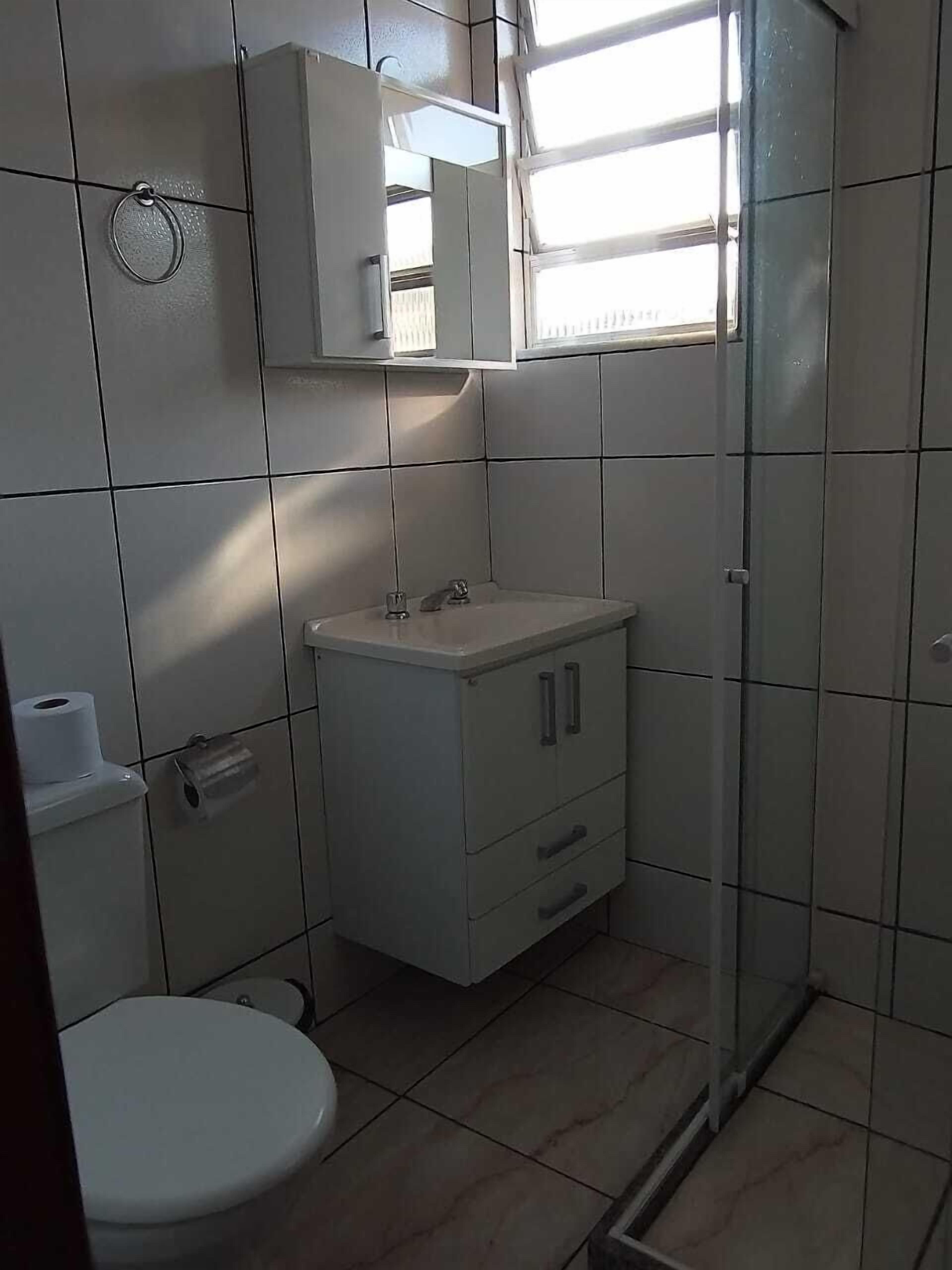 A small, tiled bathroom with a toilet, a sink, and a shower.
