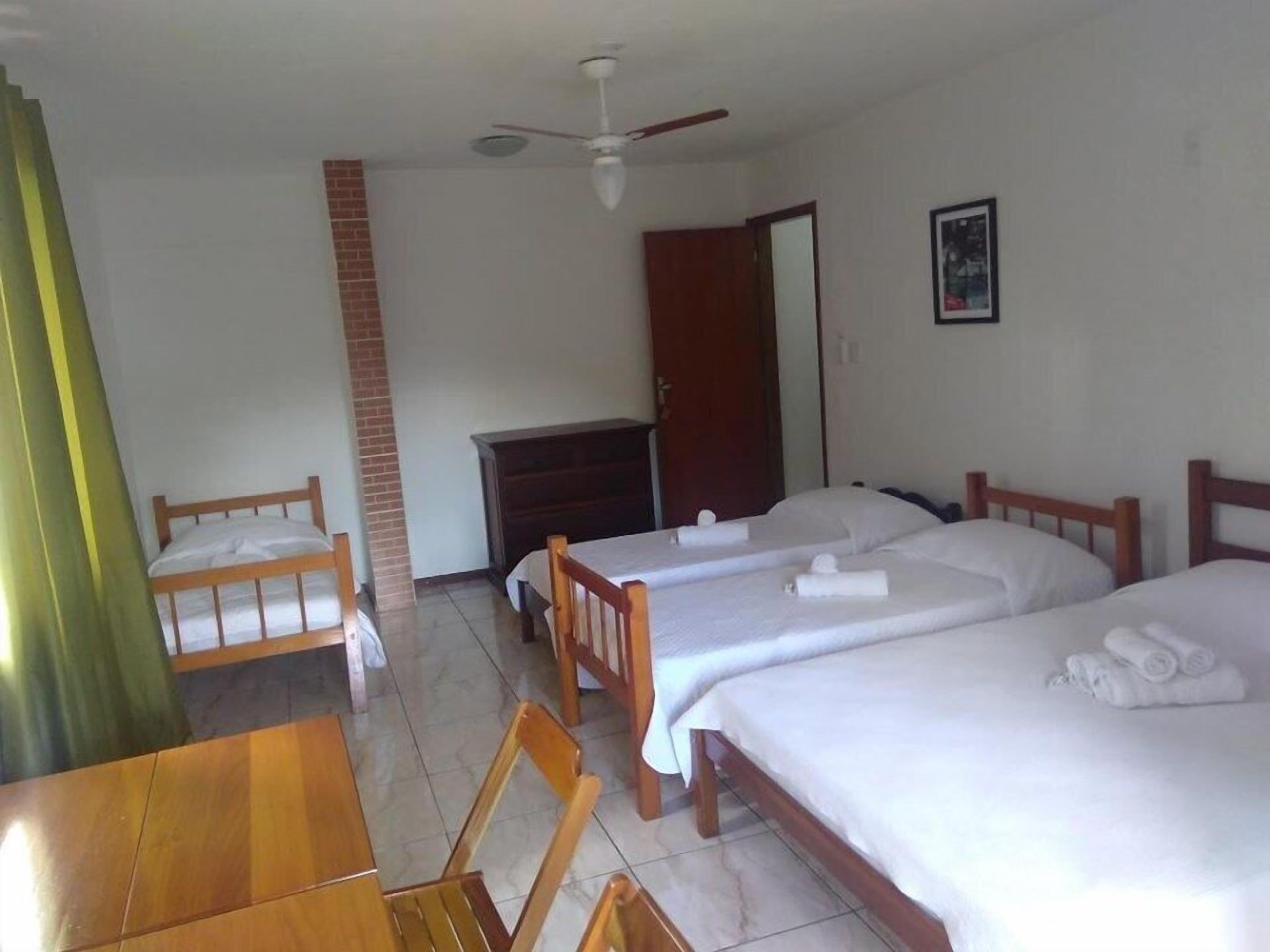 Een hotelkamer met twee bedden, een houten tafel, een stoel, een plafondventilator, een bakstenen muur en een deur.
