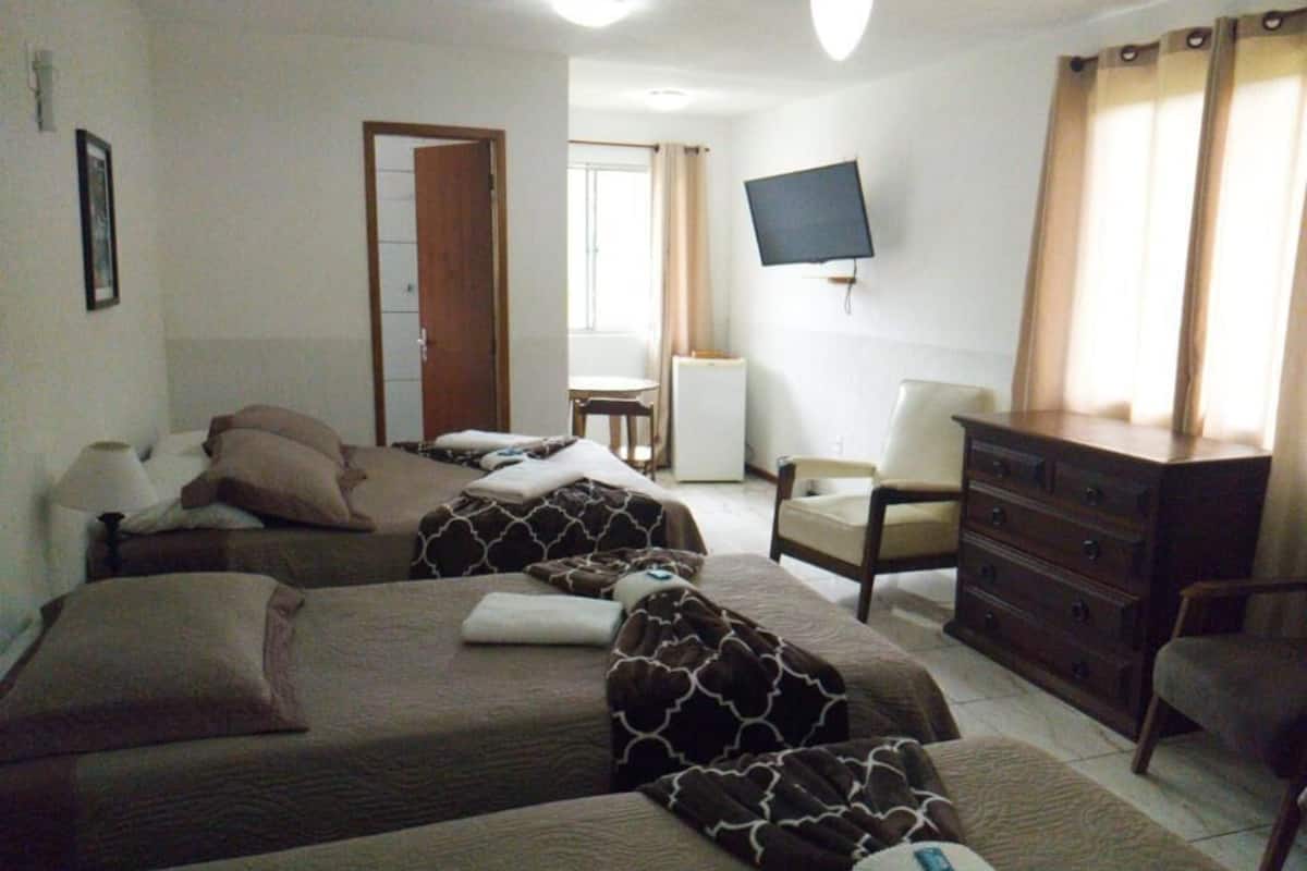 A hotel room with two beds, a desk, a chair, a dresser, a television, and a window with curtains.