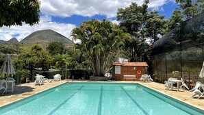 A swimming pool with lounge chairs and a small building with a sign. - Pousada Sítio Sossego (Petrópolis)