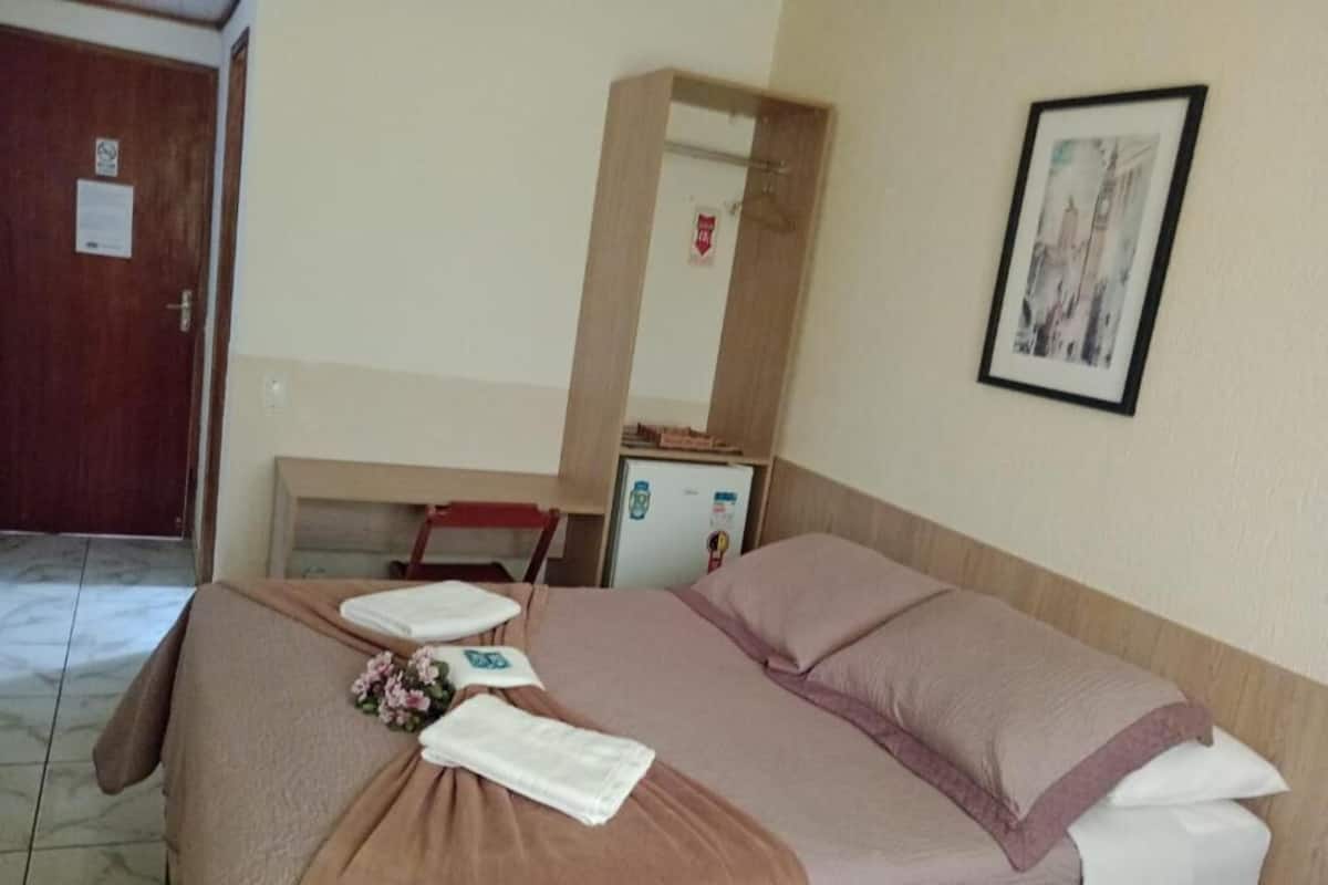 A hotel room with a bed, a desk, a mirror, and a framed picture on the wall.
