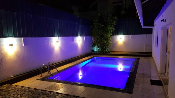 A rectangular swimming pool with a blue-lit interior, surrounded by a tiled deck and a low wall with wall-mounted lights. - Tripper's Private Villa (Negombo)