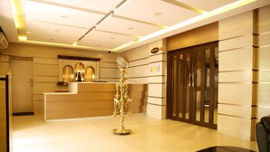 A reception area with a reception desk, a decorative golden stand, a black table, and a door with a glass panel. - Hotel Ashok Residency (Chennai)
