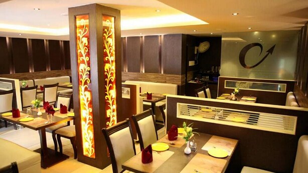 A restaurant with booths and tables, each with a menu stand and a vase with flowers. - Hotel Ashok Residency (Chennai)
