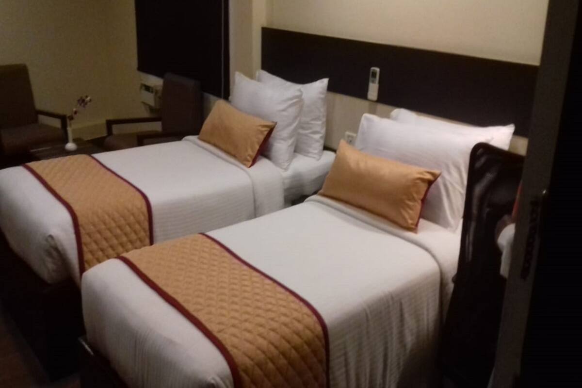 Habitación de hotel con dos camas, cada una con un cabecero acolchado y una manta color beige.