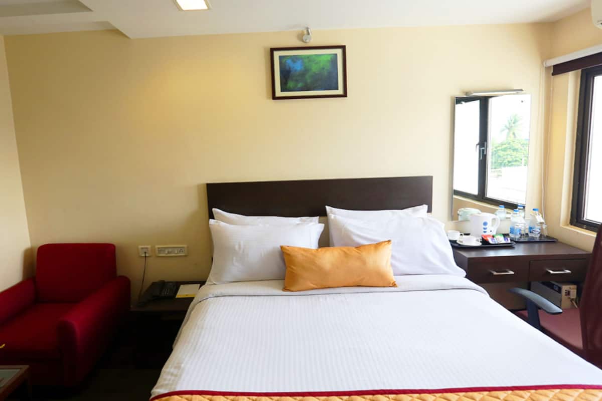 Habitación de hotel con cama, un sillón rojo, escritorio con teléfono y ventana con vista a follaje.