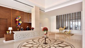 A lobby with a reception desk, a decorative wall, a patterned floor, and a large window with curtains.