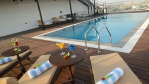 A poolside area with lounge chairs, a small table with drinks, and a view of the city skyline.