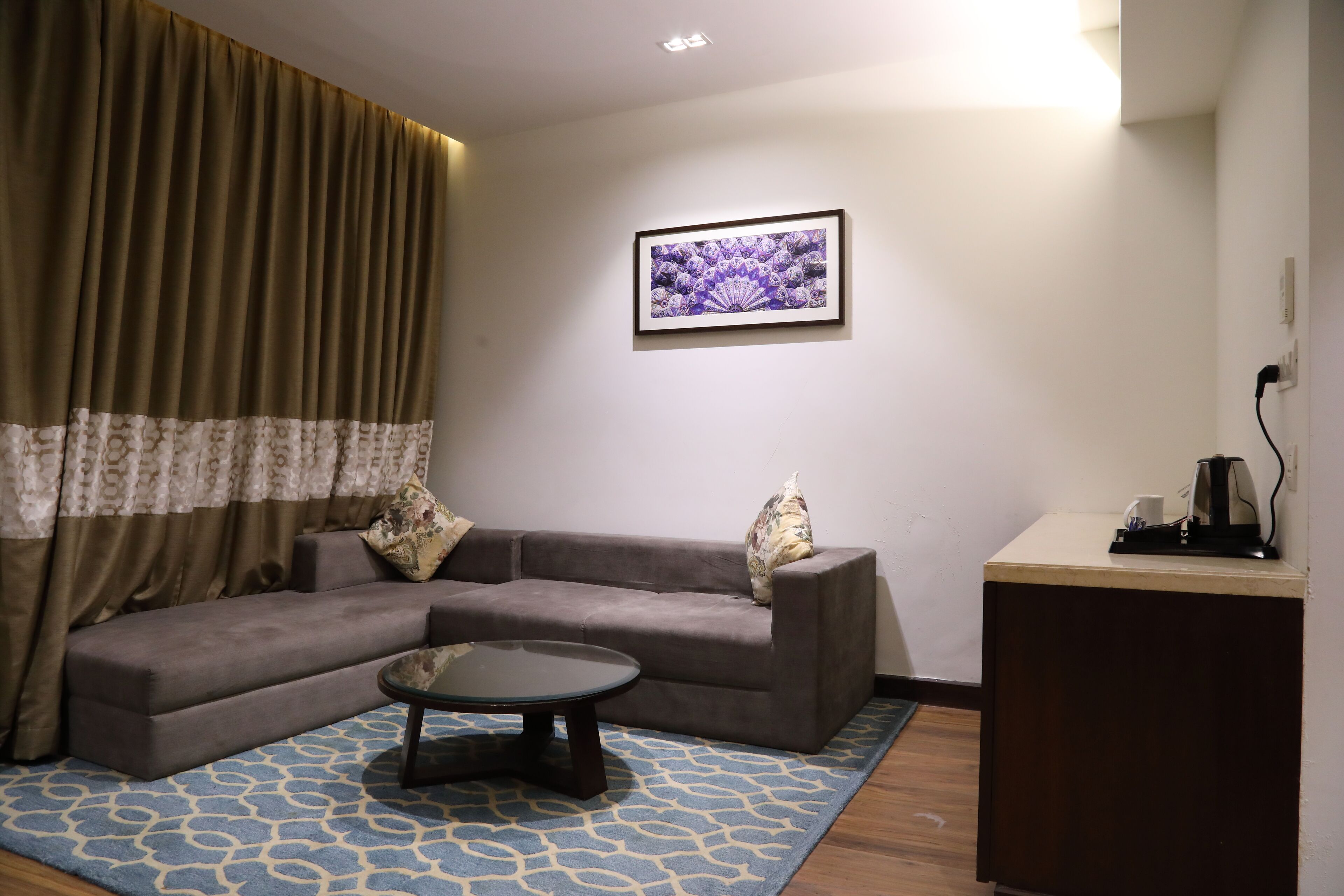 A living room with a sofa, a coffee table, a patterned rug, a wall-mounted picture, and a small cabinet.