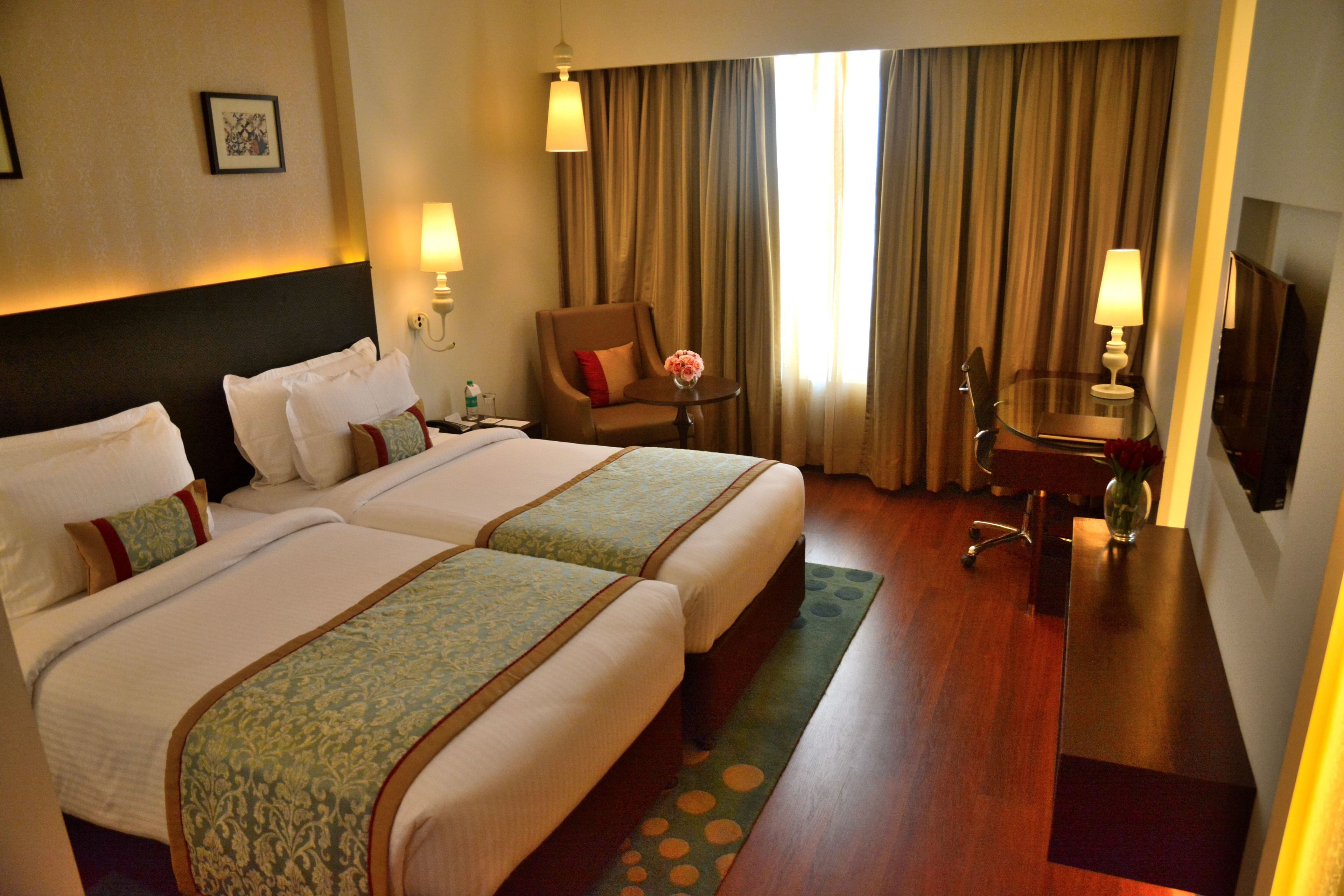 A hotel room with two beds, a chair, a table, and a TV.
