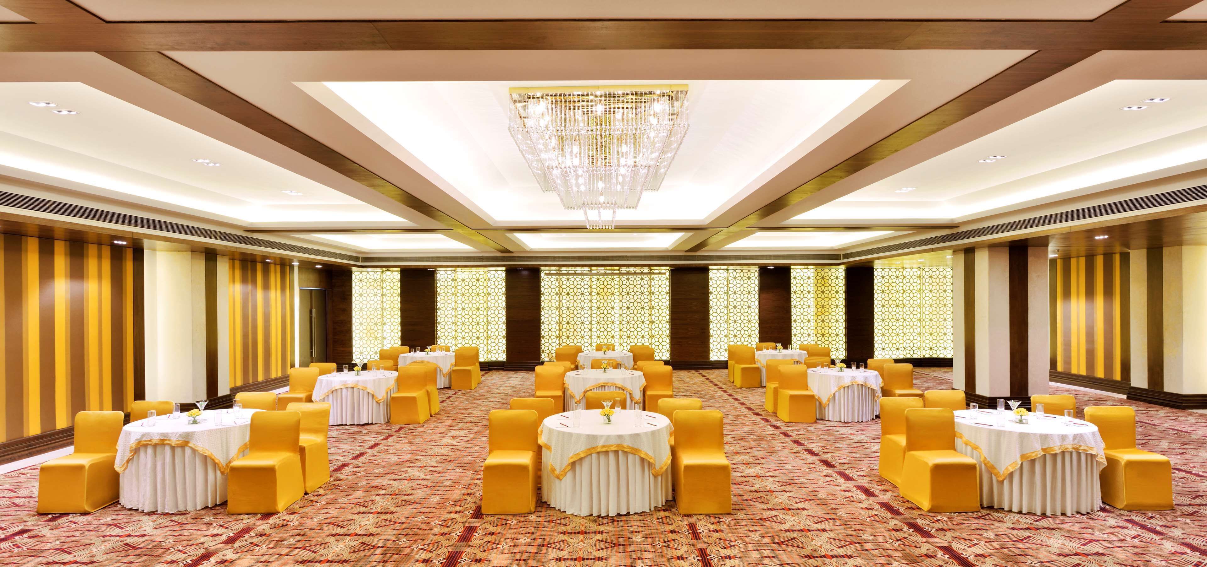 A banquet hall with round tables, yellow chairs, and a chandelier.