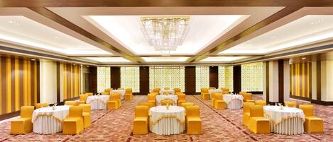 A banquet hall with round tables, yellow chairs, and a chandelier.