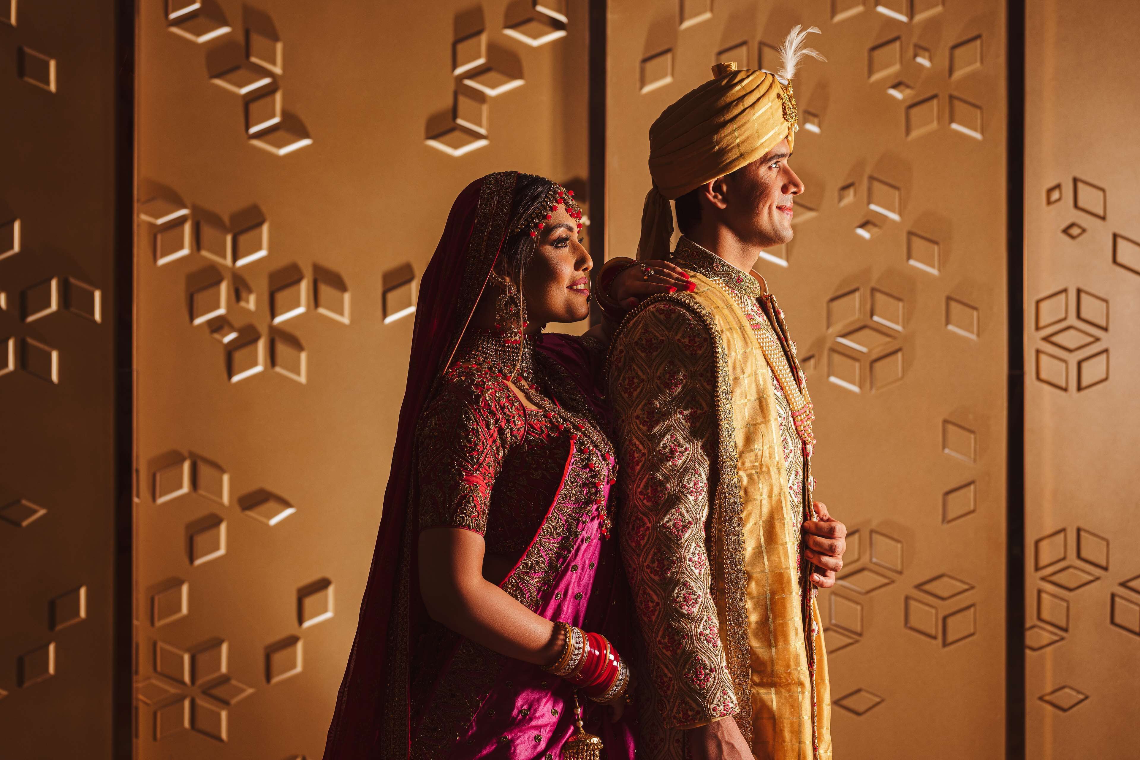 A couple in traditional attire standing in front of a geometric patterned wall.