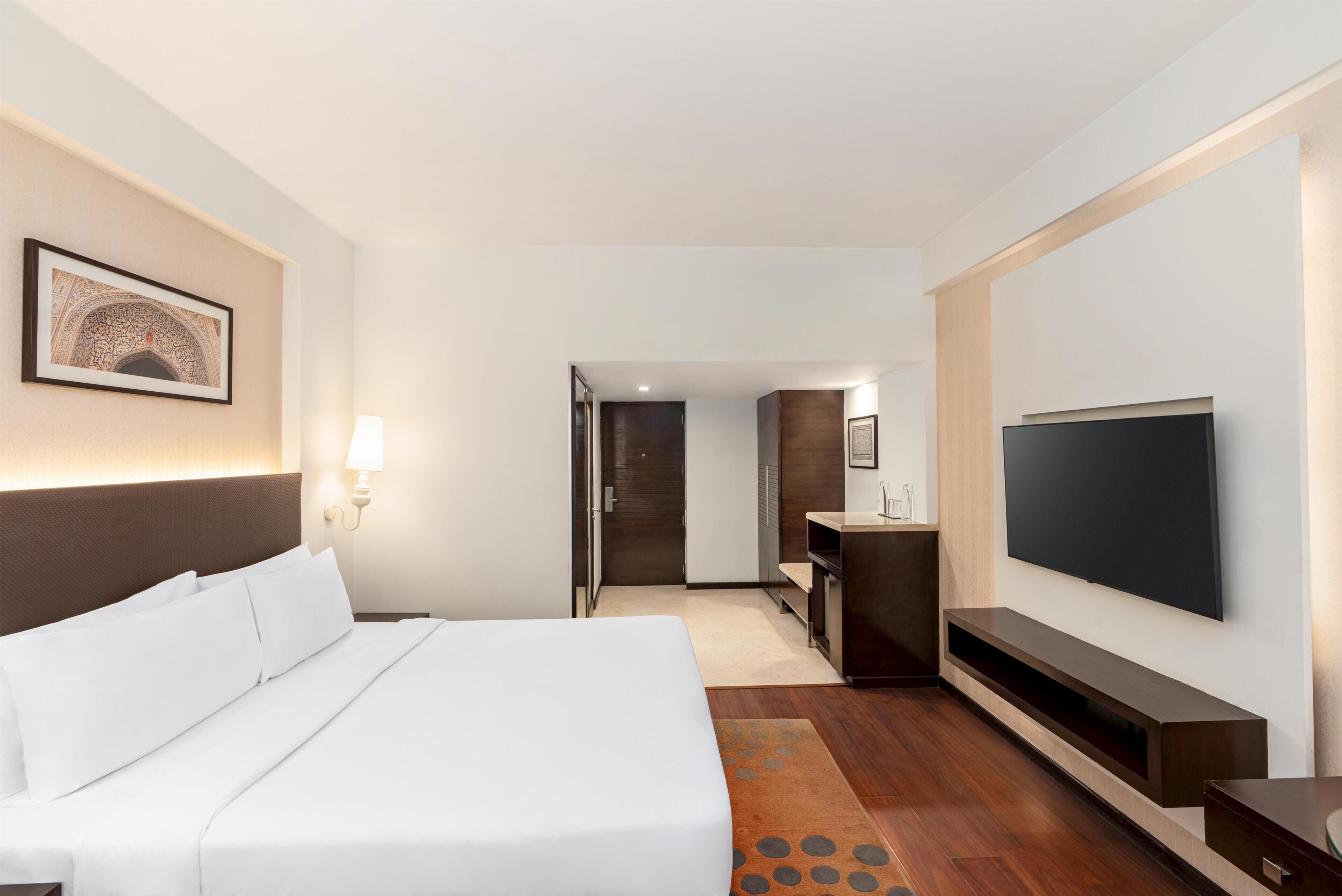 A hotel room with a bed, a TV, a desk, and a bathroom visible through an open door.