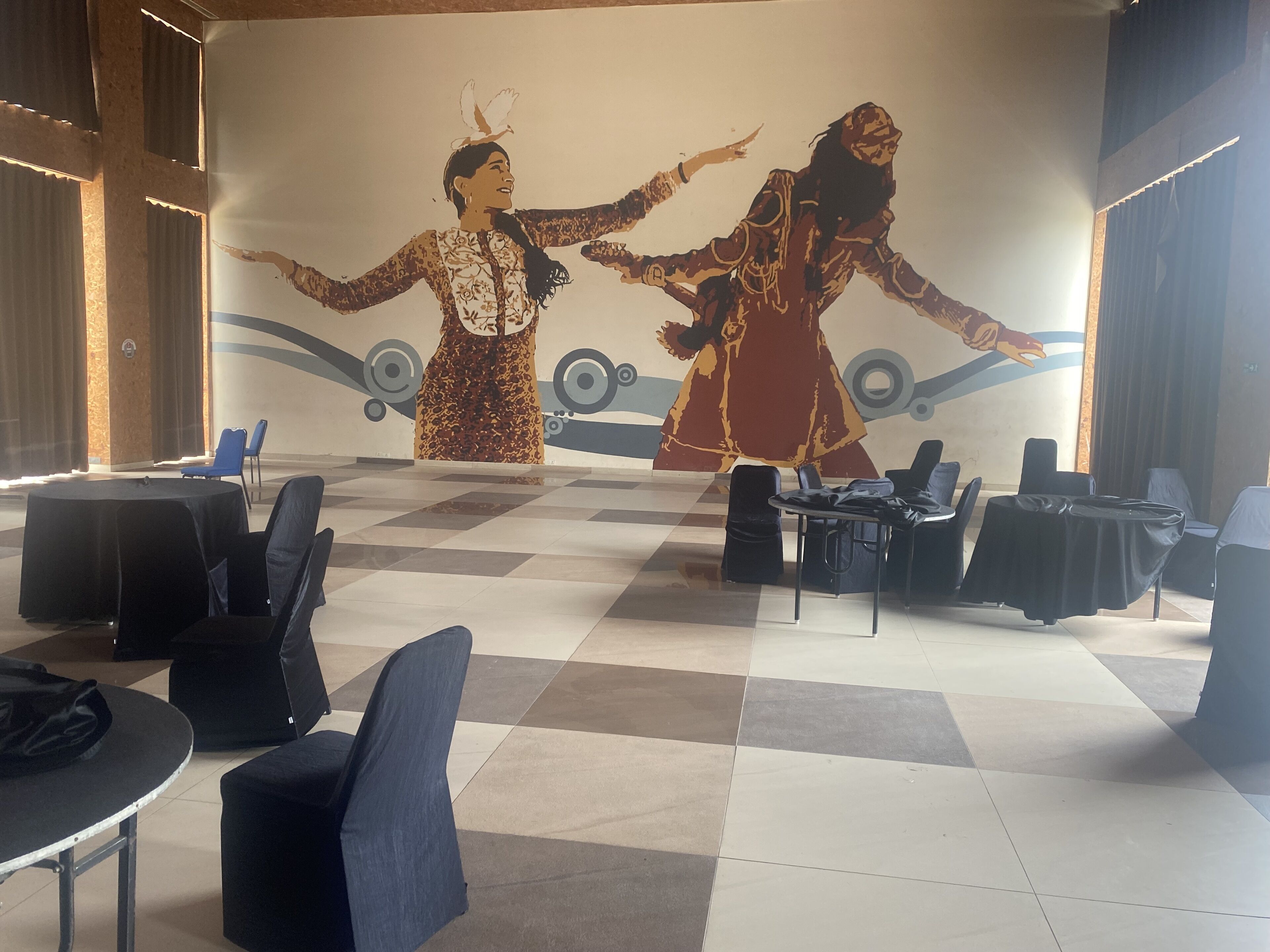 A conference room with a large mural of two figures, round tables with chairs, and a checkered floor.