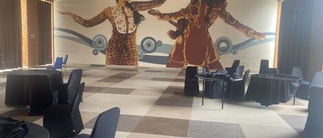 A conference room with a large mural of two figures, round tables with chairs, and a checkered floor.